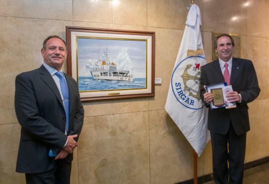 Hugo De Felice, Coordinador de Acción Cultural BCBA, recibió distinción institucional y posa junto al Prefecto Nacional Eduardo Scarzello, con la obra: "Témpanos a la deriva" de Froy de Farinon de fondo.