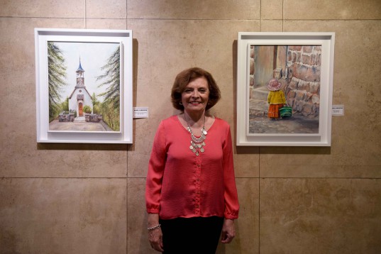 Mable Lorenzini posa entre sus obras: "Capilla de La Cumbrecita" y "De compras".